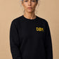 DØM black crewneck on model, yellow chest embroidery and sleeve tag