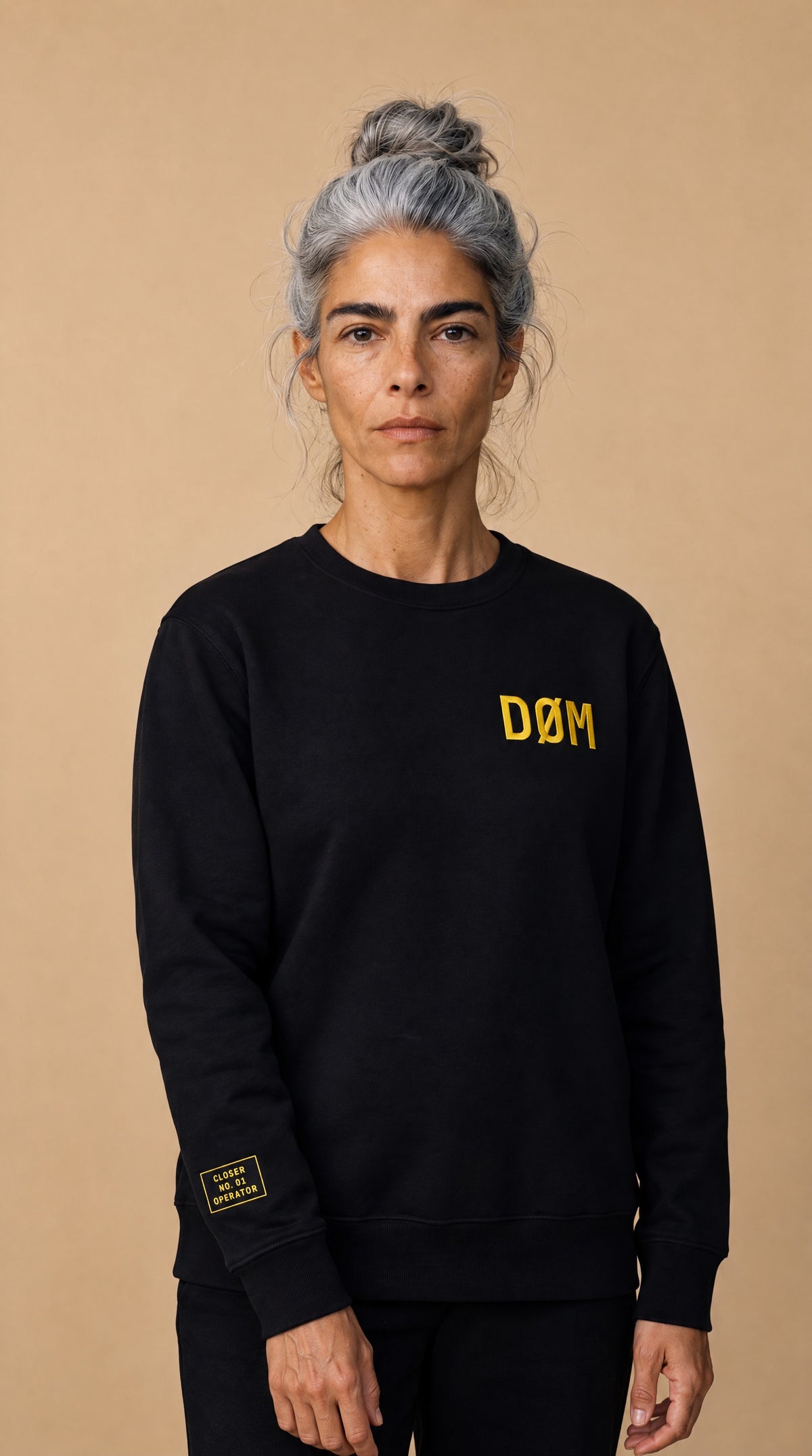 DØM black crewneck on model, yellow chest embroidery and sleeve tag